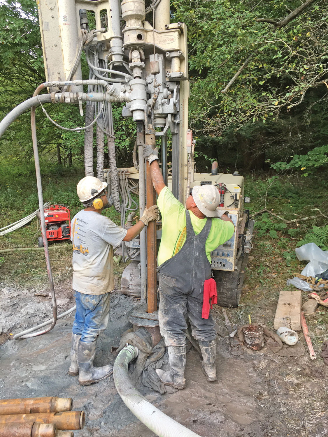 Connor Neely, driller (left), and Chris Chronister, field superintendent, add a drill rod during the 5-inch air percussion drilling as drilled water wells on site prohibiting rubber-tired vehicles.